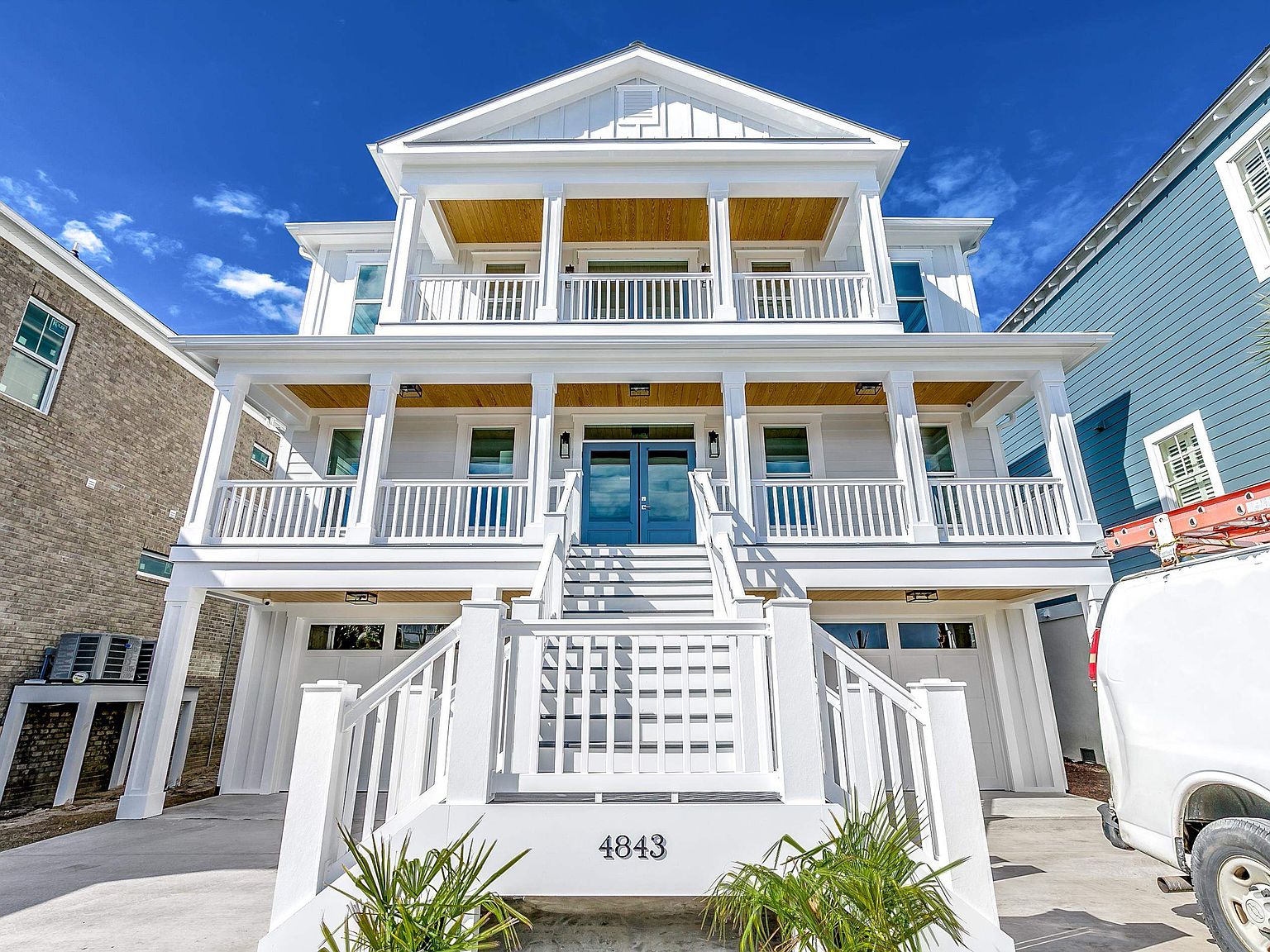 Close architectural view of 4843 , board-and-batten elevation against a deep blue sky, exposed wood porch ceilings, white columns