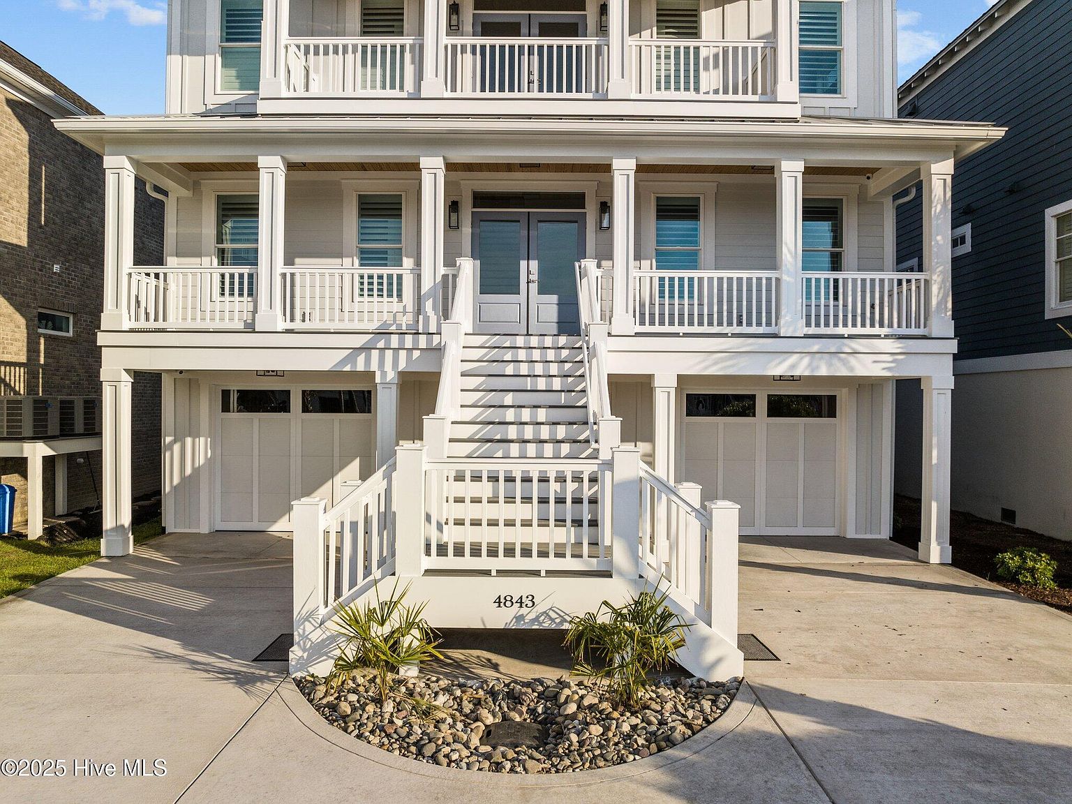 The entry detail at 4843 , the address number stamped on the foundation wall, palm fronds in the stone planter, blue front doors framed by white columns